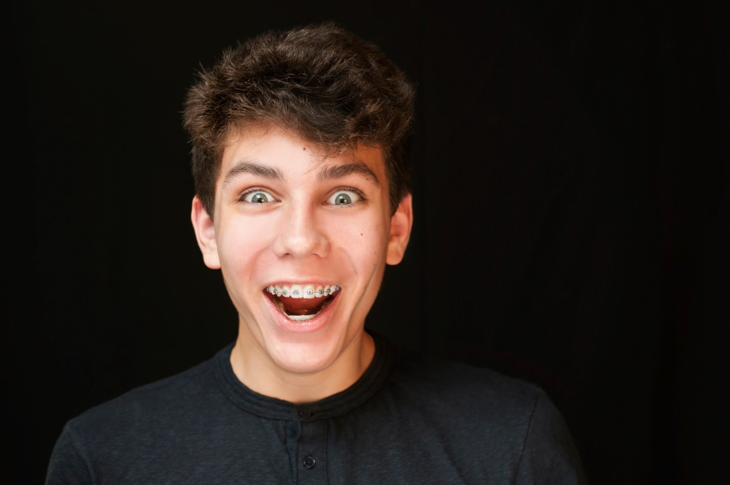 A,Boy,Of,Teenage,Age,Laughing,On,A,Black,Background.